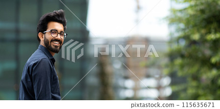 Millennial lifestyle. Career in IT tech fields. Cheerful handsome young indian guy in formal black shirt posing by business center, smiling at camera, panorama with copy space, web-banner 115635671