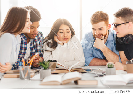 Multiracial students at a library table use books to enhance their learning. The group's dynamic interaction embodies a modern, inclusive educational environment. 115635679