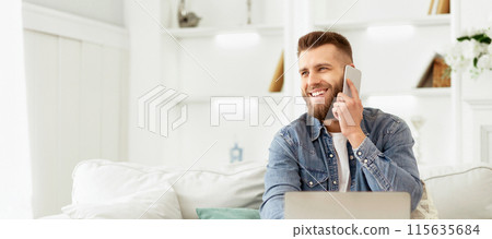 A man in casual clothing sitting on a couch indoors, engaged in a phone conversation using a mobile device. 115635684
