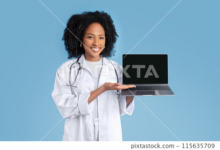 Happy young black woman doctor therapist in white coat point hand at laptop with blank screen, isolated on blue studio background. Medical, recommendation health care website, remote consultation 115635709