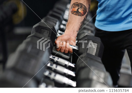 Closeup shot of muscular male arm picking up heavy dumbbell from equipment rack in modern gym, panorama 115635784