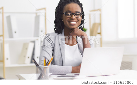 A dedicated professional black woman is working at her desk with a laptop. The office is modern and tidy, reflecting her commitment and focus on her tasks. A dedicated professional black woman is working at her desk with a laptop. The office is modern and tidy, reflecting her commitment and focus on her tasks. 115635803