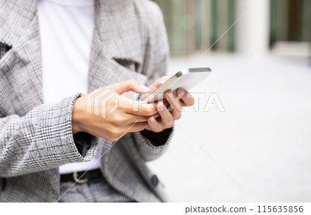 Unrecognizable businesswoman holding modern smartphone outdoors, using mobile business application, closeup with copy space. Cropped shot of young woman in suit texting on phone. Selective focus 115635856