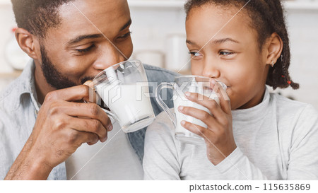 Time for vitamins. Cute Little African Girl And Her Handsome Dad Drinking Milk In Kitchen, watching each other Time for vitamins. Cute Little African Girl And Her Handsome Dad Drinking Milk In Kitchen, watching each other 115635869