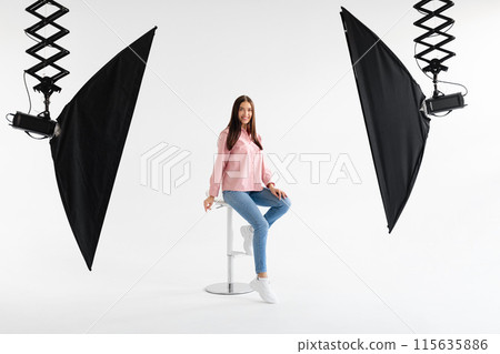 Happy european model lady in casual wear sitting on chair and posing on white background in photostudio, smiling at camera, having photoshoot and making content for shop, full length Happy european model lady in casual wear sitting on chair and posing on white background in photostudio, smiling at camera, having photoshoot and making content for shop, full length 115635886