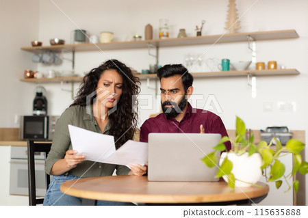 Bankruptcy concept. Overwhelmed arab couple sitting at kitchen desk in front of laptop, holding documents and reading correspondence, got mail from bank Bankruptcy concept. Overwhelmed arab couple sitting at kitchen desk in front of laptop, holding documents and reading correspondence, got mail from bank 115635888