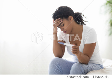 Sad young black woman checking her recent pregnancy test while sitting on bed at home, upset african american lady facing unwanted childbearing or being unable to conceive baby, having health problem Sad young black woman checking her recent pregnancy test while sitting on bed at home, upset african american lady facing unwanted childbearing or being unable to conceive baby, having health problem 115635910