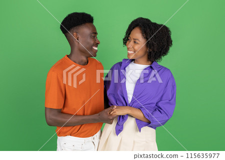 Cheerful millennial african american man and lady in casual hugging, holding hands, enjoy romantic date, isolated on green studio background. Relationship, love and walk, ad and offer 115635977