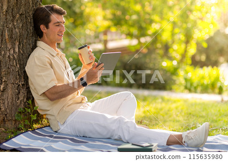 Happy handsome guy wearing casual outfit sitting under tree at public park, using digital tablet, copy space. Millennial man resting outdoors, have video call with family or lover. Telecommunication Happy handsome guy wearing casual outfit sitting under tree at public park, using digital tablet, copy space. Millennial man resting outdoors, have video call with family or lover. Telecommunication 115635980