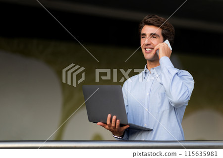 Communication in business concept. Friendly positive young entrepreneur with laptop computer in his hand have phone conversation with business partner or client, looking at copy space 115635981