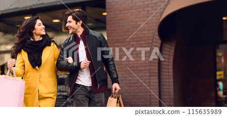 A man and woman are walking down the street, holding shopping bags in their hands. A man and woman are walking down the street, holding shopping bags in their hands. 115635989