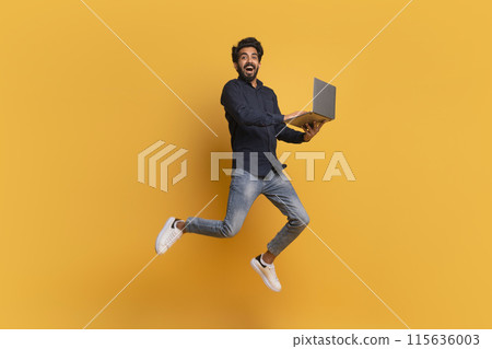 Happy indian man with laptop computer jumping up over yellow background, cheerful eastern guy using modern portable pc and flying in air, enjoying new website or online offer, full length, copy space 115636003