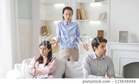 A therapist is seen mediating an intense discussion between a couple seated on a sofa in a modern living room. The couple looks upset as the therapist attempts to facilitate communication A therapist is seen mediating an intense discussion between a couple seated on a sofa in a modern living room. The couple looks upset as the therapist attempts to facilitate communication 115636048