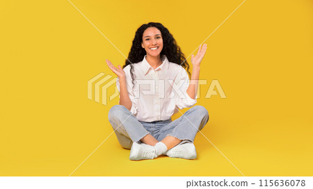 Glad Arabic Young Lady In Casual With Long Hair Sitting On Floor And Gesturing With Hands, Smiling To Camera, Expressing Positive Emotions And Advertising Nice Offer On Yellow Background. Panorama Glad Arabic Young Lady In Casual With Long Hair Sitting On Floor And Gesturing With Hands, Smiling To Camera, Expressing Positive Emotions And Advertising Nice Offer On Yellow Background. Panorama 115636078