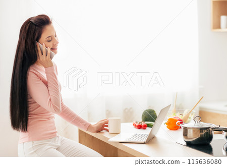 A woman is seated at a kitchen counter, engaged in conversation on a cell phone. She appears focused and attentive, possibly discussing important matters. A woman is seated at a kitchen counter, engaged in conversation on a cell phone. She appears focused and attentive, possibly discussing important matters. 115636080