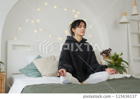 Yoga mindfulness meditation. Young healthy woman practicing yoga in bedroom at home. Woman sitting in lotus pose on bed meditating smiling relaxing indoor. Girl doing breathing practice. Yoga at home 115636137