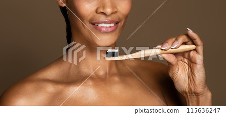Dental health. Smiling black middle aged woman holding toothbrush with toothpaste, female ready to brush her teeth, standing over brown background, panorama, cropped, closeup 115636247