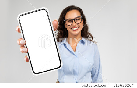 Businesswoman is seen holding a modern cell phone in her hand. The phones screen is blank, showing no content. She appears to be focused on the device, possibly waiting for a message or browsing. 115636264