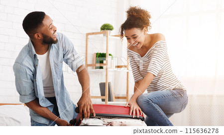 African-american couple trying to close suitcase, preparing for honeymoon 115636278