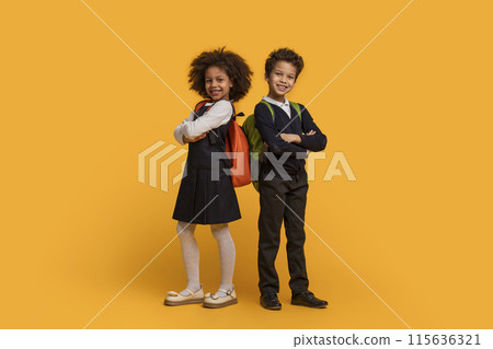 Two African American children dressed in school uniforms are standing on a bright yellow background. They appear to be waiting in line, with their eyes focused ahead Two African American children dressed in school uniforms are standing on a bright yellow background. They appear to be waiting in line, with their eyes focused ahead 115636321