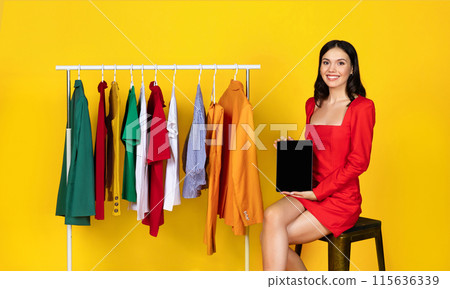 Online Shopping. Smiling Young Woman Showing Blank Digital Tablet While Sitting Near Rack With Trendy Clothes, Demonstrating Black Device Screen For Website Or App Advertisement, Mockup Online Shopping. Smiling Young Woman Showing Blank Digital Tablet While Sitting Near Rack With Trendy Clothes, Demonstrating Black Device Screen For Website Or App Advertisement, Mockup 115636339