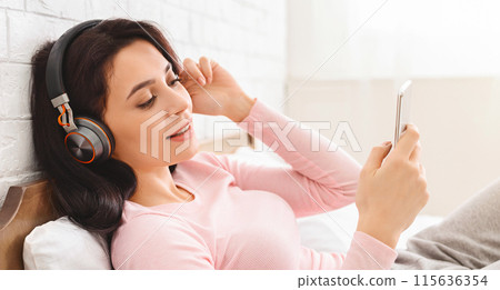 A pregnant woman is sitting down, holding her phone to her ear, listening to music with headphones on. She looks relaxed as she enjoys the music playing from her phone. A pregnant woman is sitting down, holding her phone to her ear, listening to music with headphones on. She looks relaxed as she enjoys the music playing from her phone. 115636354