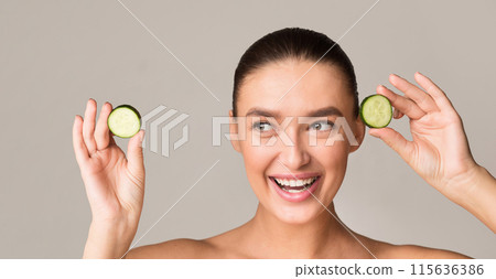 A woman is playfully holding two cucumbers up to her face, creating a humorous and lighthearted moment. The cucumbers are fresh and vibrant, contrasting with her skin tone. 115636386