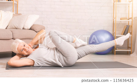 Senior woman is engaged in a yoga pose on a mat placed on the floor. She appears focused and concentrated, displaying flexibility and strength in her body movements. Senior woman is engaged in a yoga pose on a mat placed on the floor. She appears focused and concentrated, displaying flexibility and strength in her body movements. 115636425