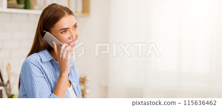 A smiling woman in a blue striped shirt talks on her phone in a kitchen. A smiling woman in a blue striped shirt talks on her phone in a kitchen. 115636462