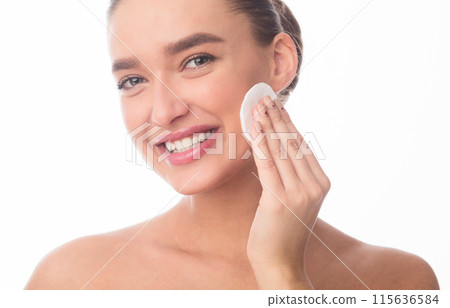 Closeup of woman is smiling as she applies facial cleanser to her skin. Her expression reflects satisfaction and relaxation while she takes care of her skincare routine. Closeup of woman is smiling as she applies facial cleanser to her skin. Her expression reflects satisfaction and relaxation while she takes care of her skincare routine. 115636584