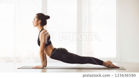 A woman is practicing a yoga pose on a green yoga mat in a fitness studio. She is fully focused and maintaining a perfect posture. A woman is practicing a yoga pose on a green yoga mat in a fitness studio. She is fully focused and maintaining a perfect posture. 115636590