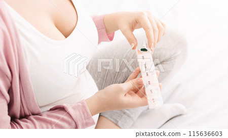 A woman is organizing her daily medication into a pillbox while sitting comfortably on a bed. She is wearing casual, home attire, with a soft focus on her hands and the pillbox, cropped A woman is organizing her daily medication into a pillbox while sitting comfortably on a bed. She is wearing casual, home attire, with a soft focus on her hands and the pillbox, cropped 115636603