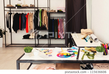 The room contains a wooden table with a stack of books and a potted plant on top. The shelf on the wall displays neatly folded clothes and a few pairs of shoes, room appears organized and functional. 115636606
