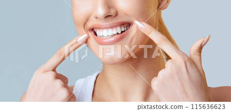 This image is a close up of a woman face. Her fingers are resting on her cheeks, and she is smiling widely, showing off her bright white teeth, cropped 115636623