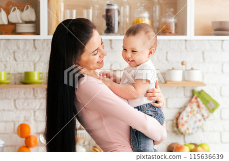 A woman is holding a baby in her arms, cradling the infant gently as they share a moment of bonding and care. The woman expression shows love and tenderness towards the baby 115636639