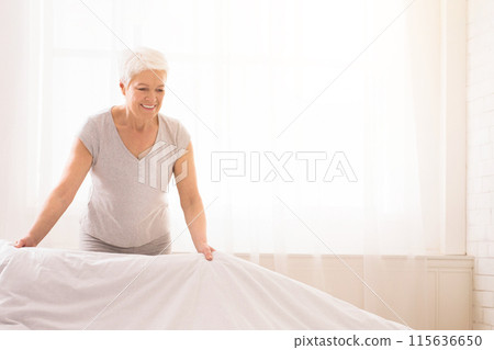 A cheerful, elderly woman is in the process of making her bed with a sense of care and attention in a brightly lit bedroom, copy space A cheerful, elderly woman is in the process of making her bed with a sense of care and attention in a brightly lit bedroom, copy space 115636650