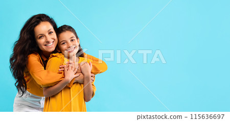 Beautiful european mother hugging her daughter and smiling at camera on blue studio background, panorama with copy space. Parenthood, motherhood, family concept Beautiful european mother hugging her daughter and smiling at camera on blue studio background, panorama with copy space. Parenthood, motherhood, family concept 115636697