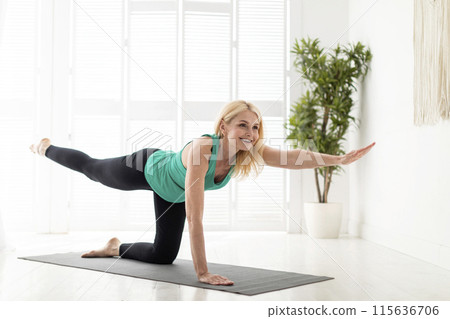 Beautiful mature lady in sportswear doing morning yoga, making bird dog pose, smiling senior woman training on fitness mat at home, stretching opposite leg and arm, enjoying healthy lifestyle 115636706