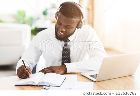 Looking for inspiration. Creative black businessman listening to music with wireless headset at workplace, planning future Looking for inspiration. Creative black businessman listening to music with wireless headset at workplace, planning future 115636762