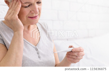 Senior woman is seen holding a thermometer in her hand, likely checking her temperature for any signs of fever or illness, closeup 115636875