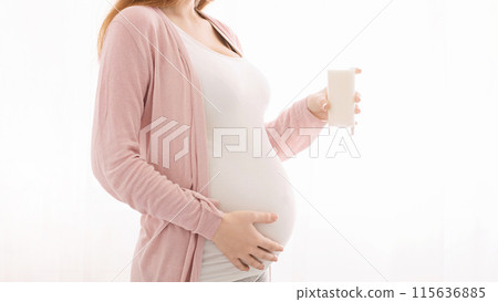 A pregnant woman, with a noticeable baby bump, is standing while holding a glass of milk in her hand, showcasing the healthy beverage choice she is making during her pregnancy, cropped A pregnant woman, with a noticeable baby bump, is standing while holding a glass of milk in her hand, showcasing the healthy beverage choice she is making during her pregnancy, cropped 115636885