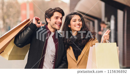 A man and a woman standing together, holding shopping bags in their hands. A man and a woman standing together, holding shopping bags in their hands. 115636892