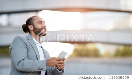 Smiling Handsome Young Businessman With Smartphone In Hands Standing Outdoors And Looking Aside At Copy Space, Millennial Male Entrepreneur In Suit Holding Mobile Phone, Enjoying Modern Communication Smiling Handsome Young Businessman With Smartphone In Hands Standing Outdoors And Looking Aside At Copy Space, Millennial Male Entrepreneur In Suit Holding Mobile Phone, Enjoying Modern Communication 115636969