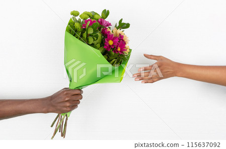 Hand of young african american guy gives bouquet of flowers to woman isolated on white studio background, close up. Surprise, love and relationship, birthday, anniversary, holiday celebration Hand of young african american guy gives bouquet of flowers to woman isolated on white studio background, close up. Surprise, love and relationship, birthday, anniversary, holiday celebration 115637092