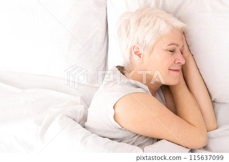 A woman is lying down in bed, covered by crisp white sheets. She appears relaxed and comfortable, with her eyes closed, possibly resting or sleeping, view above A woman is lying down in bed, covered by crisp white sheets. She appears relaxed and comfortable, with her eyes closed, possibly resting or sleeping, view above 115637099