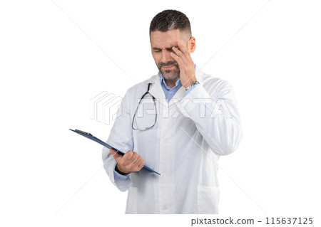 A man doctor, wearing a white lab coat, looks concerned as he reviews patient records on a clipboard. He is pressing his temple with one hand, indicating possibly a headache or concentration. 115637125
