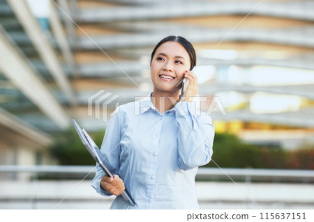 An Asian businesswoman in professional attire is engaged in a phone conversation. She appears focused and attentive while speaking into her smartphone, possibly discussing work-related matters. An Asian businesswoman in professional attire is engaged in a phone conversation. She appears focused and attentive while speaking into her smartphone, possibly discussing work-related matters. 115637151