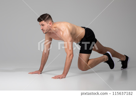 A man is performing push ups on a gray background. He is using his hands and feet to lift and lower his body repeatedly in a strength-building exercise. 115637182