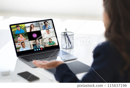 A businesswoman is seen hosting a virtual team meeting on her laptop in a bright office during the morning. Her colleagues are visible on the screen, engaged and participating in the discussion. A businesswoman is seen hosting a virtual team meeting on her laptop in a bright office during the morning. Her colleagues are visible on the screen, engaged and participating in the discussion. 115637196