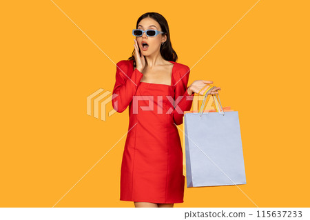 A young woman, dressed in a stylish red dress and blue sunglasses, stands against a vibrant yellow backdrop, her mouth open in a surprised expression. A young woman, dressed in a stylish red dress and blue sunglasses, stands against a vibrant yellow backdrop, her mouth open in a surprised expression. 115637233